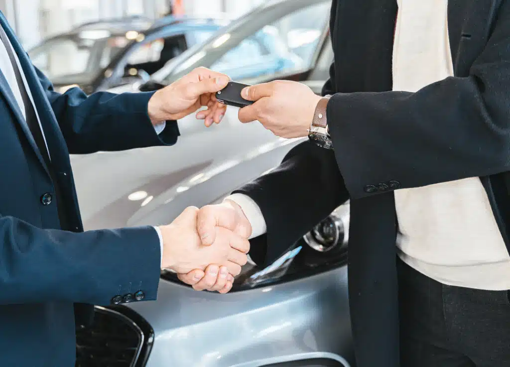 Automotive dealership professional handing car keys to a client while shaking hands, symbolizing successful partnership and business growth supported by Strativera.